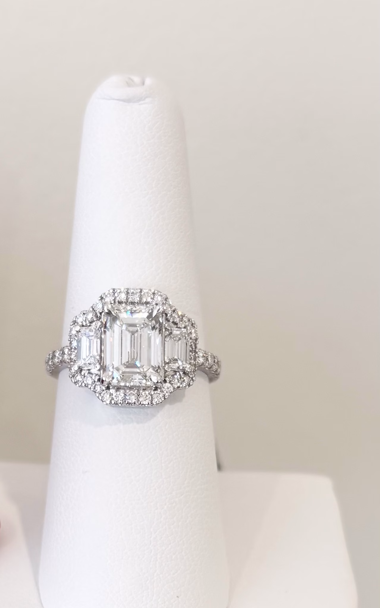 14K white gold emerald cut diamond ring with halo, side emerald cut diamonds, and diamond band.